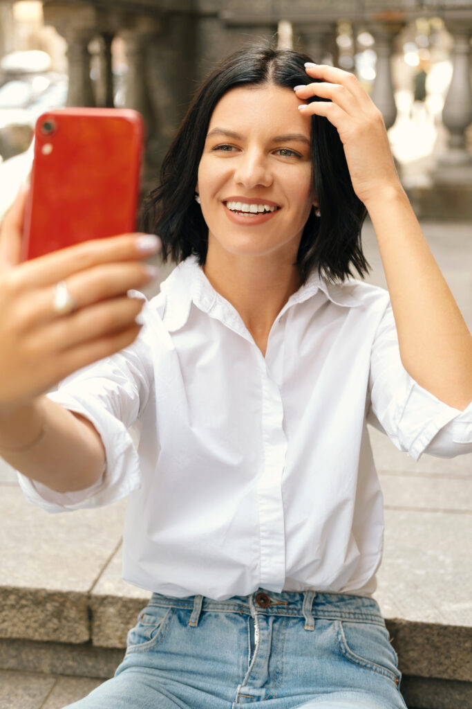 Vertical Photo Of Young Beautiful Woman In Casual Sitting On Stairs In Old City And Taking Selfie With Smartphone