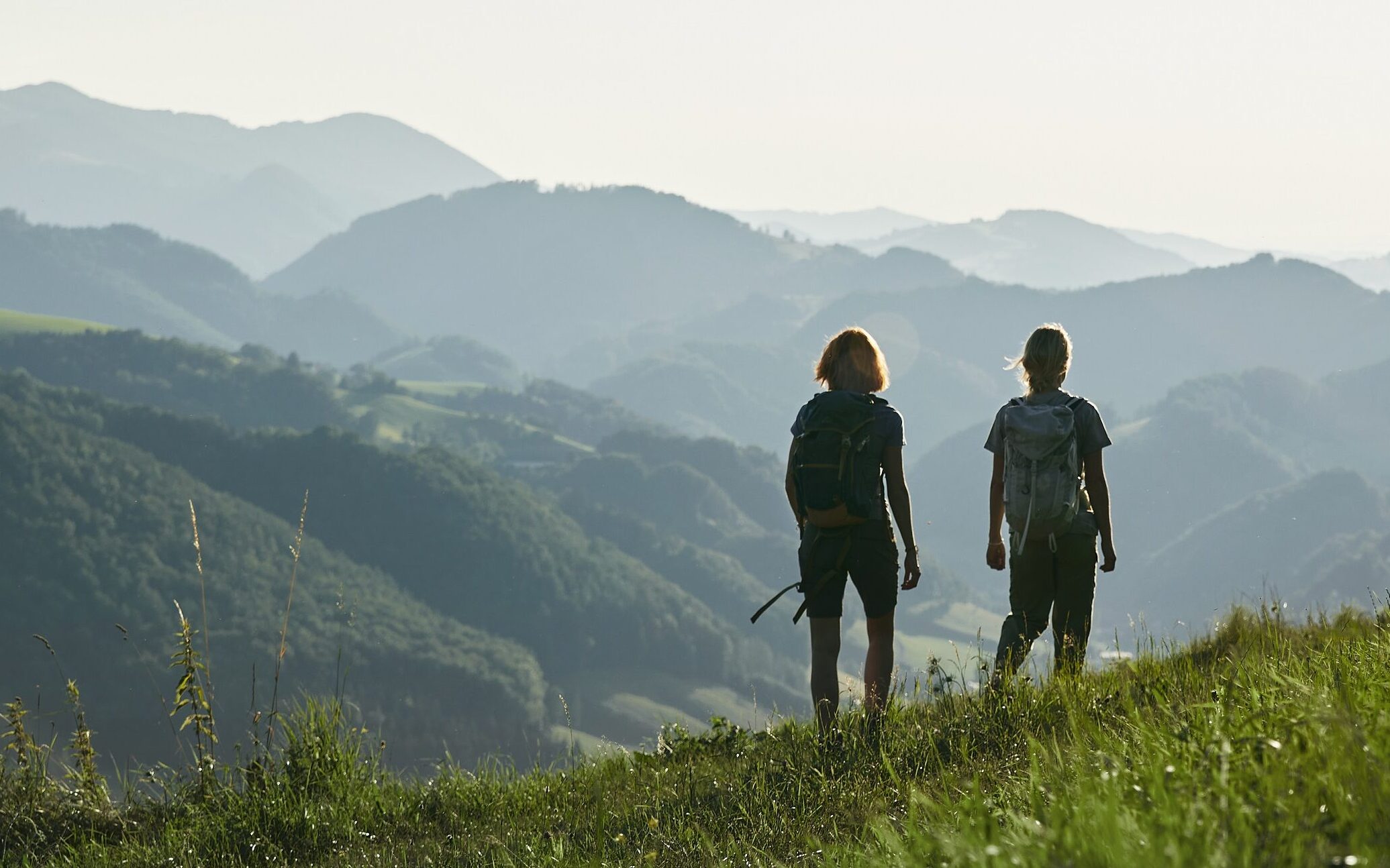 Zwei junge Frauen wandern auf einer Wiese, im Hintergrund das Ennstal. Nationalparkregion wandern Sebaldusweg © Oberoesterreich Tourismus GmbH Stefan Mayerhofer